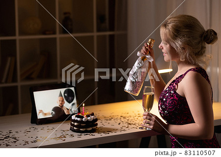 Birthday celebration. Online greeting. Virtual friends. Happy festive woman cheering champagne looking male congrats on laptop in dark room interior. 83110507