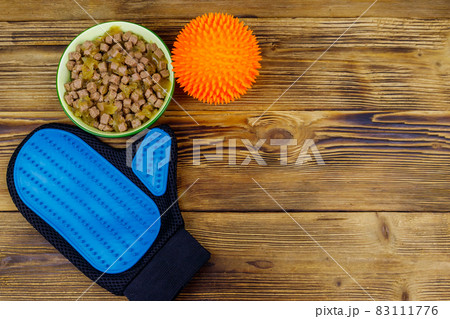 Canned dog food in bowl, ball toy and pet grooming glove on wooden background. Top view, copy space. Pet care concept Canned dog food in bowl, ball toy and pet grooming glove on wooden background. Top view, copy space. Pet care concept 83111776
