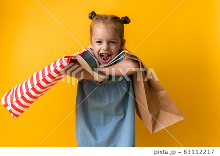 Portrait Caucasian Beautiful Happy Little Preschool Girl Smiling Cheerful And Holding Heavy Cardboard Bags Isolated On Orange Yellow Background. Happiness, Consumerism, Sale People shopping Concept 83112217