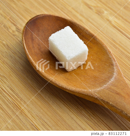 White and sugar cubes in wooden spoon on bamboo cutting board 83112271