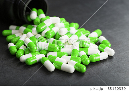 A pattern of green and white medical pills on a black background. A pattern of green and white medical pills on a black background. 83120339