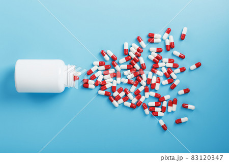 A scattering of red and white tablets capsules from a white jar on a blue background. 83120347