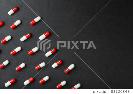 A pattern of red and white pill capsules on a black background background. A pattern of red and white pill capsules on a black background background. 83120348