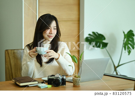 Attractive young woman holding cup of hot coffee and reading news on laptop computer. Attractive young woman holding cup of hot coffee and reading news on laptop computer. 83120575