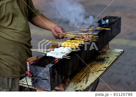 Man grilling skewered meat on a street barbecue stall in Beijing, China Man grilling skewered meat on a street barbecue stall in Beijing, China 83120786