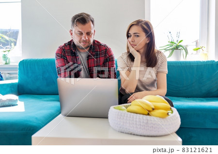 Serious middle aged couple looking at laptop screen at home in living room 83121621