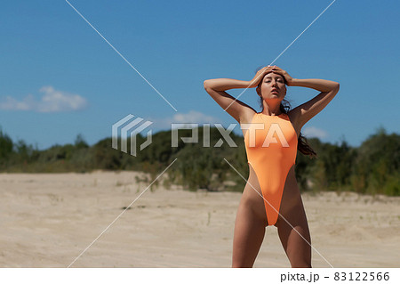 Young woman in orange swimsuit standing on sand Young woman in orange swimsuit standing on sand 83122566