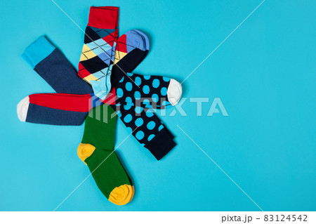 Several colored socks with different patterns, lined with a flower shape on a green leg, on a cyan background, lifestyle concept Several colored socks with different patterns, lined with a flower shape on a green leg, on a cyan background, lifestyle concept 83124542