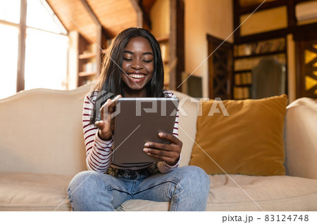 Happy young black lady using tablet, learning or working remotely, having online video call, sitting on sofa indoors 83124748