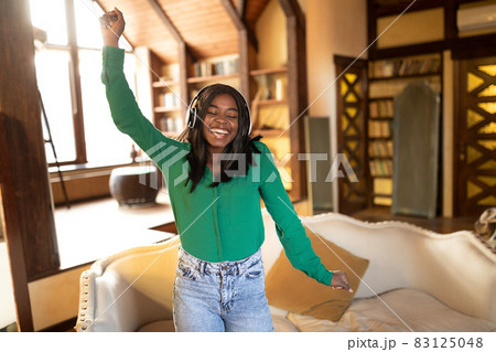 Happy young African American lady with wireless headphones dancing to beautiful music at home, copy space Happy young African American lady with wireless headphones dancing to beautiful music at home, copy space 83125048