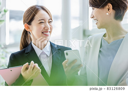職場でスマホを見ながら立ち話をする2人のビジネスウーマン 83126809