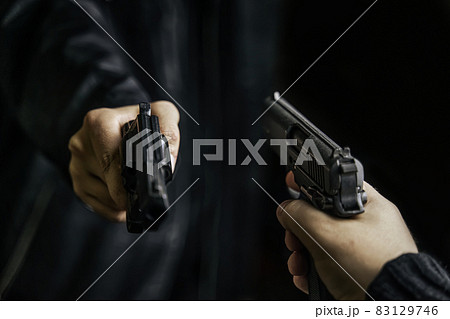Two men's hands with weapons pointed at each other. 83129746