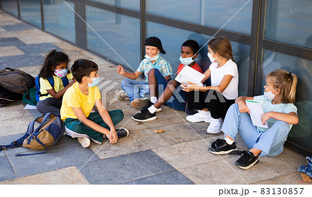 Preteen children in face masks resting in schoolyard during break Preteen children in face masks resting in schoolyard during break 83130857