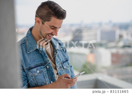 Portrait of young caucasian man with smartphone standing on balcony. 83131665