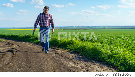 a man as a farmer walking along the field, dressed in a plaid shirt and jeans, checks and inspects young sprouts crops of wheat, barley or rye, or other cereals, a concept of agriculture and agronomy a man as a farmer walking along the field, dressed in a plaid shirt and jeans, checks and inspects young sprouts crops of wheat, barley or rye, or other cereals, a concept of agriculture and agronomy 83132056