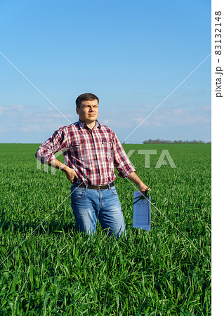 a man as a farmer poses in a field, dressed in a plaid shirt and jeans, checks reports and inspects young sprouts crops of wheat, barley or rye, or other cereals, a concept of agriculture and agronomy a man as a farmer poses in a field, dressed in a plaid shirt and jeans, checks reports and inspects young sprouts crops of wheat, barley or rye, or other cereals, a concept of agriculture and agronomy 83132148