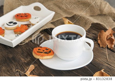 Autumn composition of orange and white cookies for Halloween, cups of fragrant black coffee stands on brown wooden table Autumn composition of orange and white cookies for Halloween, cups of fragrant black coffee stands on brown wooden table 83132838