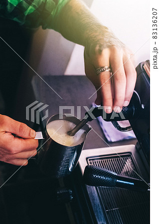 Close-up of a barista preparing coffee. The process of making cappuccino in a coffee machine. Measuring cup in hand. The hot drink is poured into a paper cup. Takeaway food 83136207