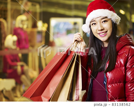 happy young asian woman wearing christmas hat carrying shopping bags happy young asian woman wearing christmas hat carrying shopping bags 83138562