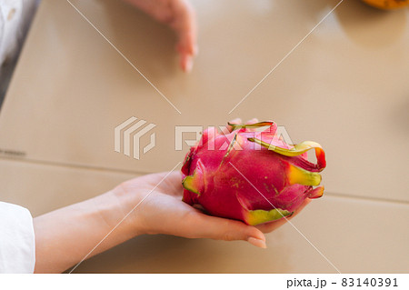 Close-up top view of unrecognizable young woman holding in hands Pitaya dragon fruit sitting at wooden table in kitchen room. 83140391