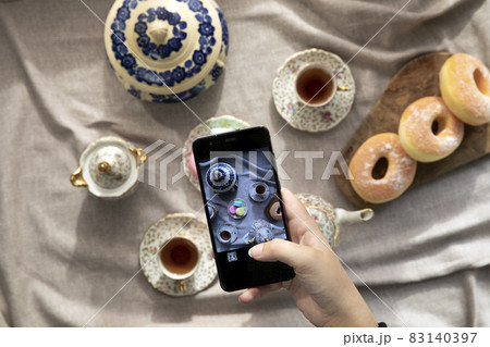 Top view picture of lady,blogger sitting in cafe and making photo with mobile of food, afternoon tea with doughnuts and macarons on the table high angle, food and social media concept Top view picture of lady,blogger sitting in cafe and making photo with mobile of food, afternoon tea with doughnuts and macarons on the table high angle, food and social media concept 83140397