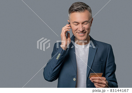 Man with smartphone near ear looking at credit card 83144167