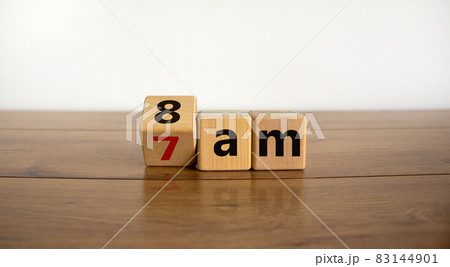 Concept for getting up early in the morning. Turned a cube and changed the alarm time from 7 am to 8 am or vice versa. Beautiful wooden table, white background. Copy space. 83144901