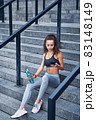 Young athletic woman in sport clothes sitting on stairs of city stadium with phone in hands posting her training results 83148149