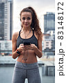 Young athletic woman in sport clothes standing on city background with phone in hands posting her training results 83148172