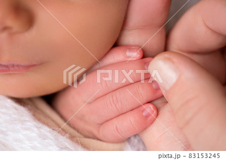 Happy mom lovingly hold the fingers of a newborn baby in a soft grey plaid  83153245