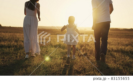 a little laughing girl runs with her parents at sunset, a happy family, a childhood dream, kid running in sunshine with mom and dad, playing catch-up with child, father and mother with baby daughter 83155655