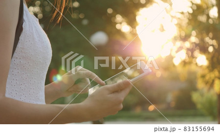 A young girl holds in her hand a modern tablet in the glare of the sunset, go online to the Internet, the rays of the sun shine on the touch screen of the tablet, the concept of modern technologies 83155694