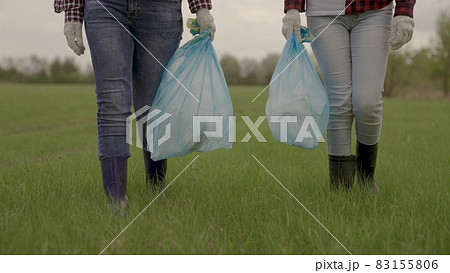A man carries garbage in garbage bags on green grass, collection and disposal of unnecessary waste, a woman in gloves for cleaning work, help protecting the planet's environment, clean earth 83155806