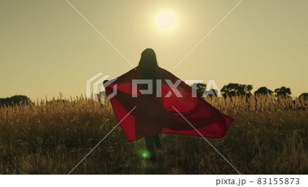 happy girl play superheroes they run across green field in red cloak, cloak flutters in wind. children's games and dreams. Slow motion. teenager dreams of becoming superhero. young girls in red cloak 83155873