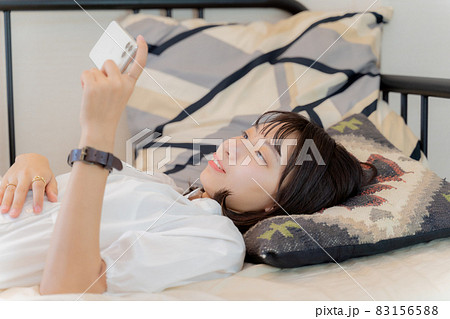 ベッドで仰向けでスマホを見る女性の写真素材 [83156588] - PIXTA