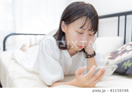頬杖ついてベッドでスマホを眺める女性 頬杖ついてベッドでスマホを眺める女性 83156596