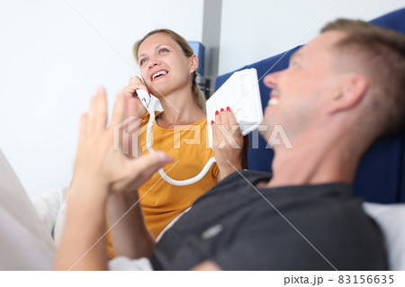 Woman is talking on phone while lying with man on bed in hotel room 83156635
