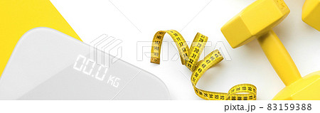 Flat lay top view scales, dumbbell and tape measure on white yellow background 83159388