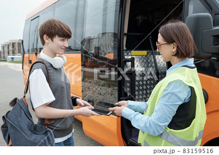 Happy girl passenger holding smartphone under tablet of young female bus conductor Happy girl passenger holding smartphone under tablet of young female bus conductor 83159516