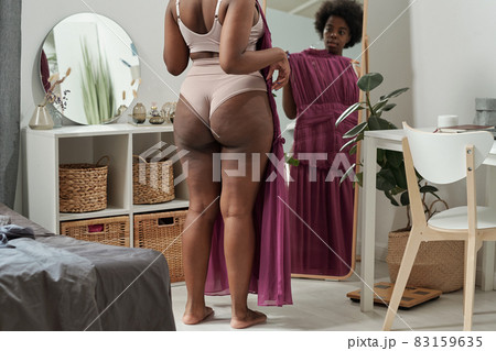 Rear view of young plus size woman trying on new dress 83159635