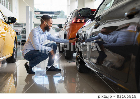 Black Male Customer Choosing New Automobile In Dealership Center, Examining Wheel Rims 83165919