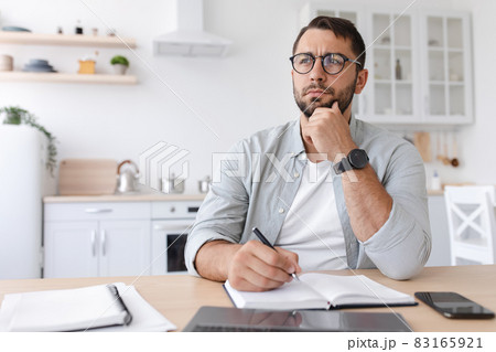 Pensive adult caucasian guy teacher or businessman with beard in glasses makes notes, works at laptop 83165921
