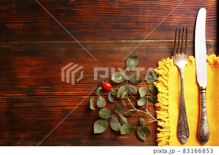 Thanksgiving table setting concept. Fork and knife with dog-rose leaves and berries on brown wooden table. November mood background with briar branches. Copy space, close up, top view, flat lay. Thanksgiving table setting concept. Fork and knife with dog-rose leaves and berries on brown wooden table. November mood background with briar branches. Copy space, close up, top view, flat lay. 83166853