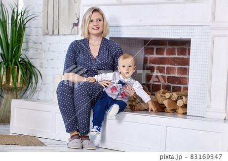 Toddler with mother sit in lounge near fireplace. 83169347
