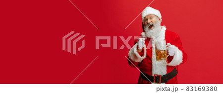 Cropped portrait of senior man wearing Santa Claus costume, holding lager foamed beer glass. Oktoberfest. Flyer Cropped portrait of senior man wearing Santa Claus costume, holding lager foamed beer glass. Oktoberfest. Flyer 83169380
