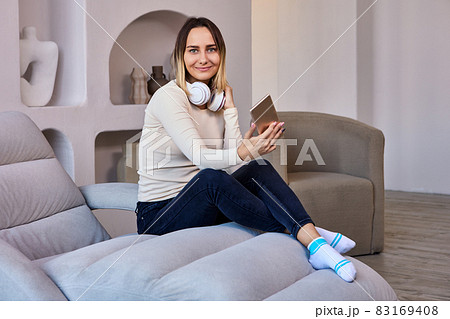 Lounge where woman on sofa and in headphones holds phone. 83169408