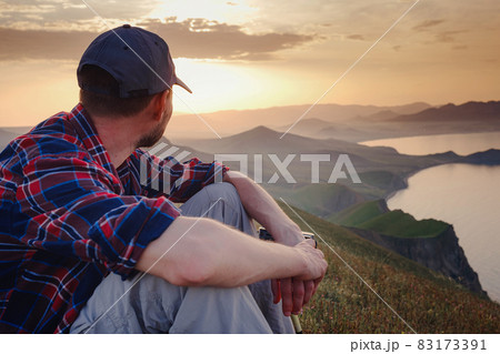 Confident man sitting and enjoying view in hilly landscape Confident man sitting and enjoying view in hilly landscape 83173391