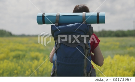 Young millennial girl travels with backpack and tourist rug, bright day in life, happy vacation concept, nature vacation on tourist road, looking for adventure on vacation, traveler concept 83173967
