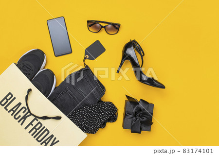 Paper shopping bag with clothes spill out on yellow background. Black friday concept. Paper shopping bag with clothes spill out on yellow background. Black friday concept. 83174101