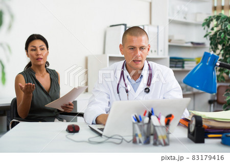 Doctor writing prescription to female patient on laptop at clinic Doctor writing prescription to female patient on laptop at clinic 83179416